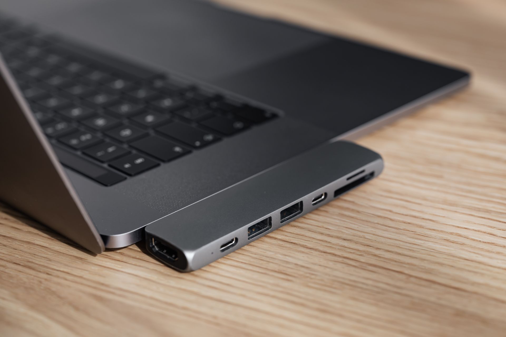 A sleek modern laptop connected to a USB hub, placed on a wooden desk, showcasing connectivity and tech innovation.