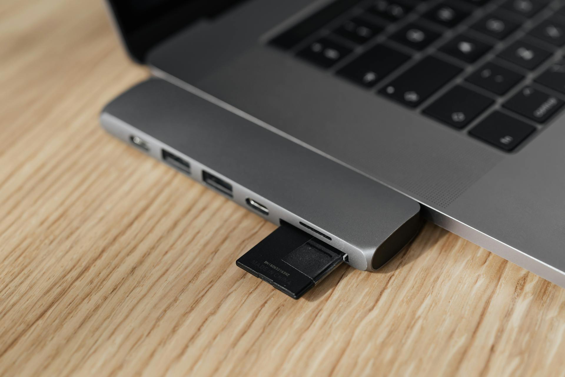 Close-up of a modern laptop with memory card adapter connected on a wooden desk.