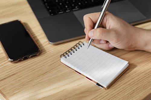 Free Crop person writing in notebook at workplace Stock Photo