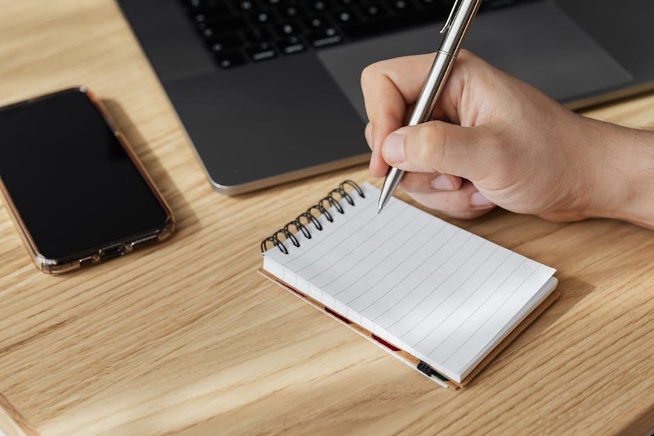 Crop person writing in notebook at workplace