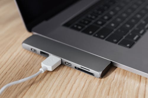 High angle of modern space silver laptop with USB type c multiport hub with plugged white cable placed on wooden table