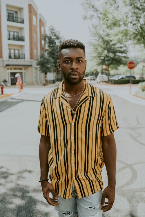 Free Young African American guy in bright shirt with stripes looking at camera while standing on road Stock Photo