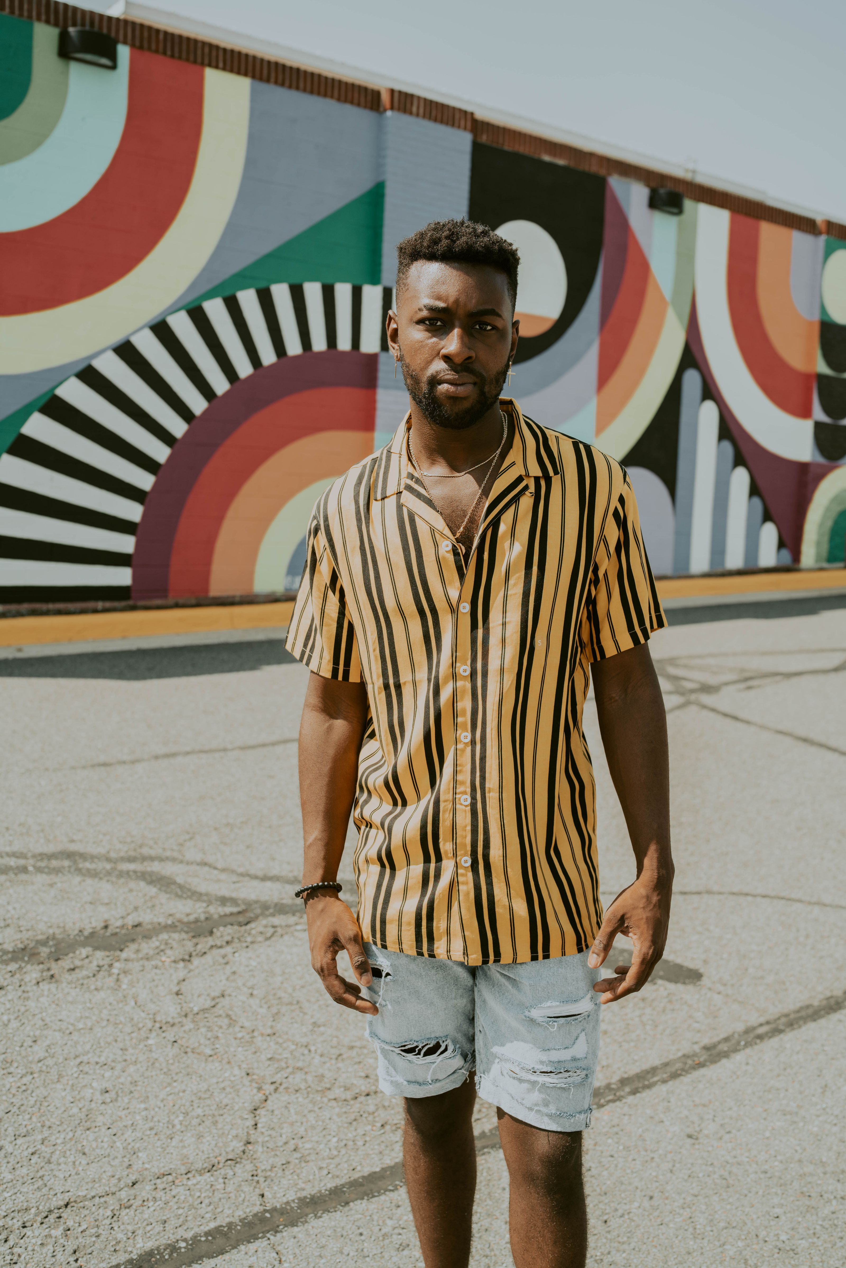 Homem moderno em uma camisa listrada posando em frente a uma parede de graffiti colorida em um dia ensolarado.