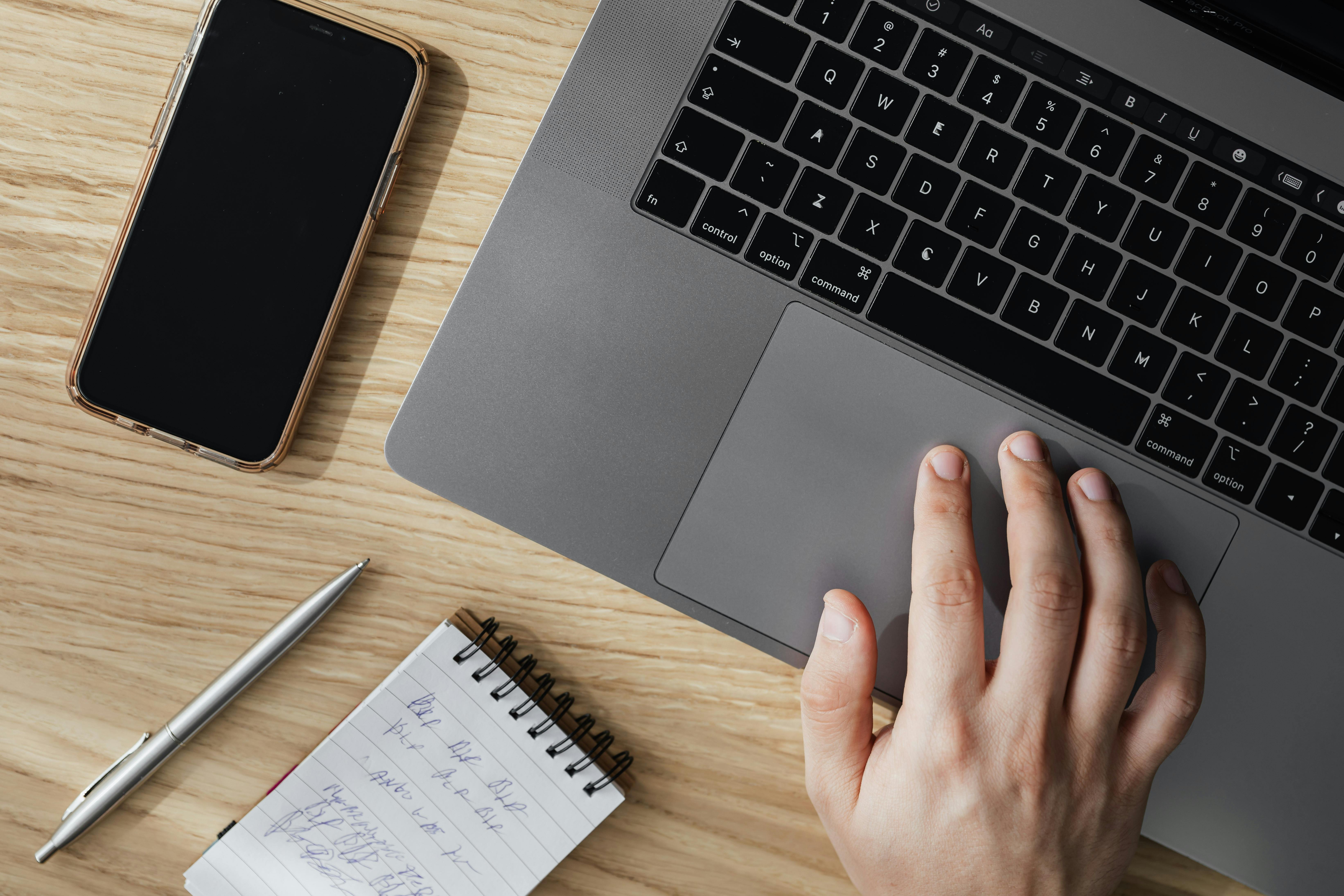 crop person working on laptop at table with smartphone and notepad