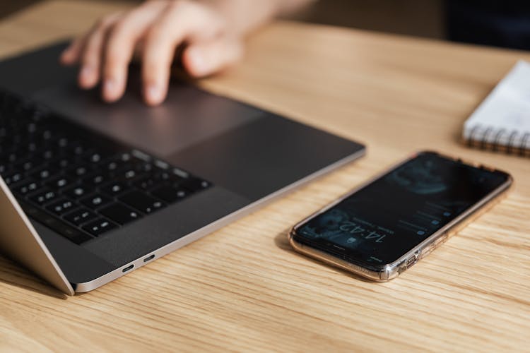 Crop Person Using Touchpad On Laptop At Table With Smartphone