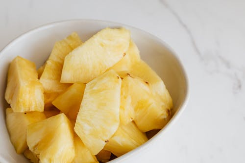 From above of fresh pieces of ripe pineapple served in white deep plate and placed on marble table