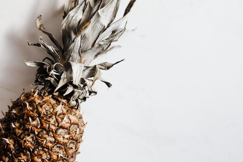Top view of ripe whole pineapple with dried crown placed on white background