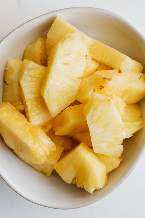 From above of pieces of fresh pineapple placed in white bowl on white marble table