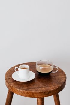 靠近白墙的圆形木桌上，放着陶瓷白杯和宽玻璃杯中的新鲜咖啡
