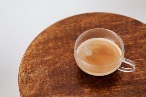 From above of coffee with thin froth in glass cup placed on small round wooden table on white background