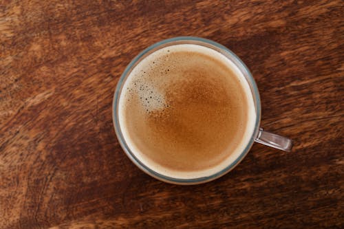 Free Top view of coffee with thin foam in glass cup standing on brown wooden table Stock Photo