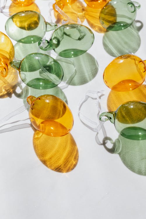 From above of decorative shiny yellow and green transparent glass baubles lying on white surface in sunlight