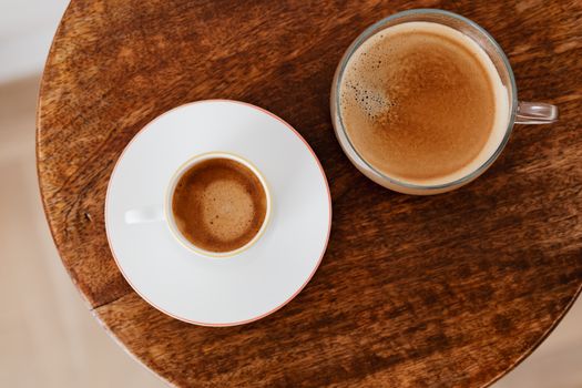 茶碟上的白杯咖啡和圆形木桌上宽玻璃杯中的咖啡