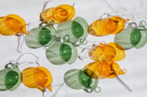 Top view of decorative yellow and green transparent glass baubles with white ribbons lying on white table and glistening in sun