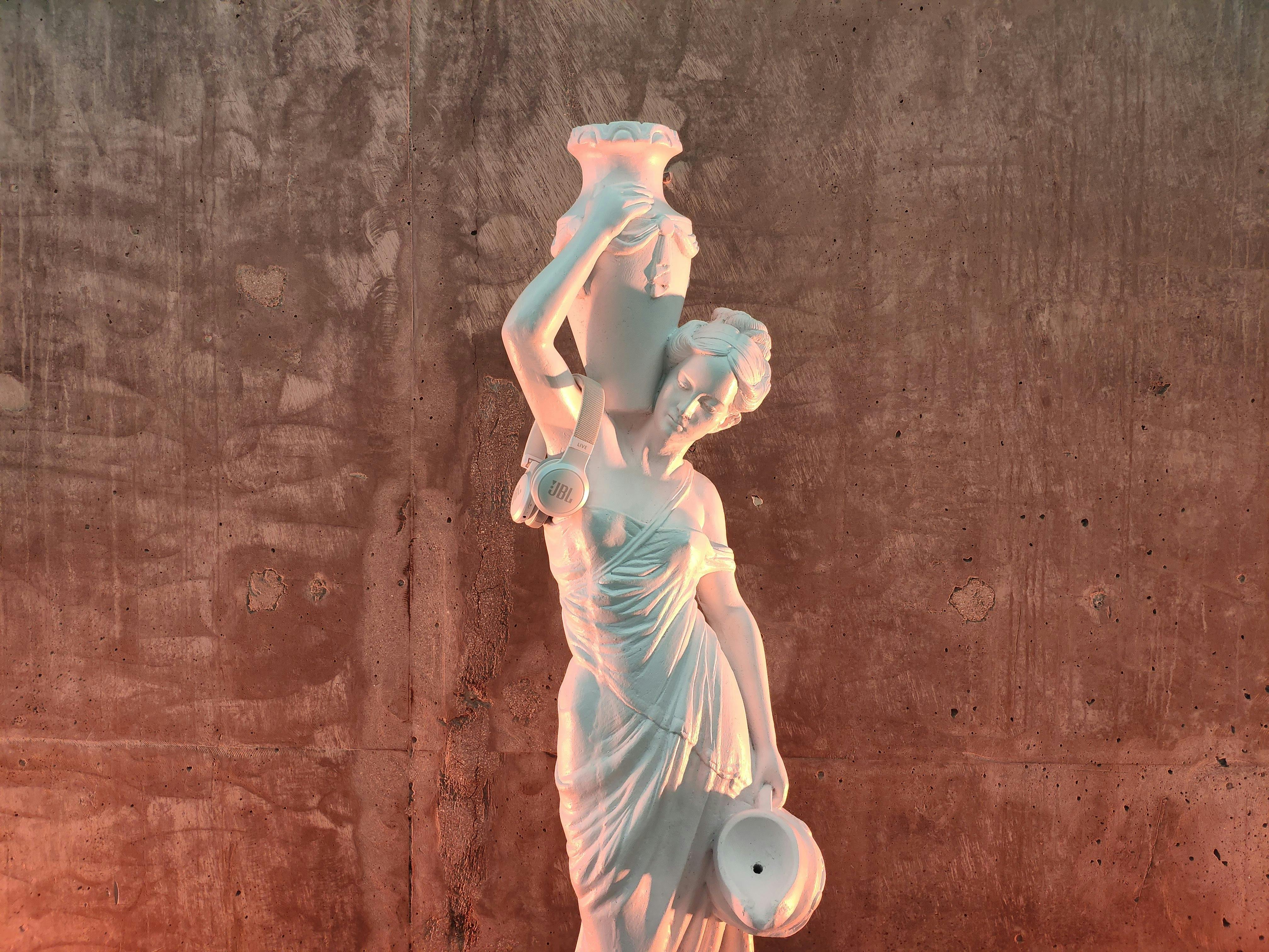 Aged masonry sculpture of female carrying decorative jug on shoulder and contemporary headphones near shabby wall
