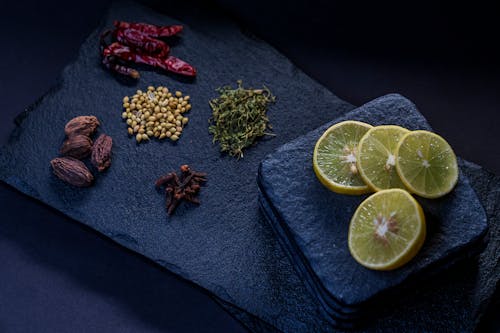 Free From above of dried chili peppers near thyme and pine nuts with cloves and ripe lemon slices on stone board Stock Photo