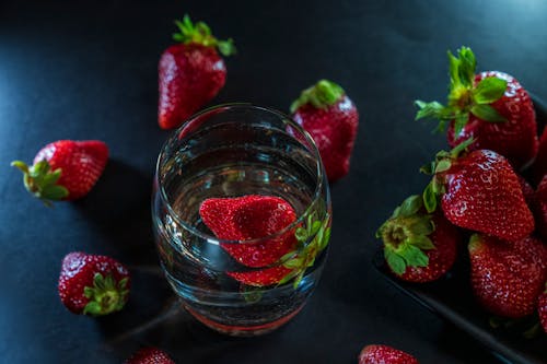 From above of transparent glass with water and bright fresh strawberries with green sepals on table