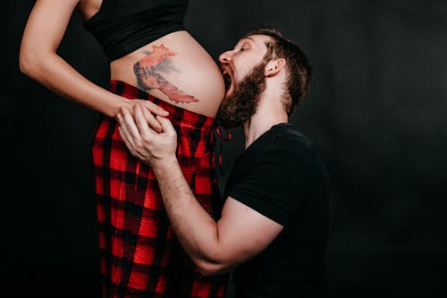 Free Hipster man biting belly of unrecognizable expectant beloved with tattoo Stock Photo