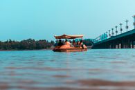 Low angle of anonymous travelers on boat with roof sailing on wavy lake near bridge under blue sky