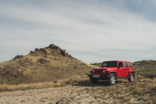 A red SUV parked on rugged terrain with a rocky hill under a bright sky, symbolizing adventure travel.