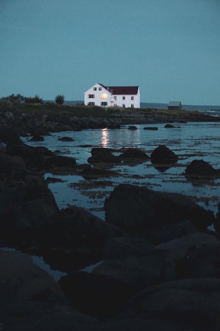 House With Shiny Light Reflecting In Lake At Night