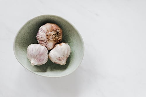 Top view of ceramic bowl of garlic bulbs standing on white marble table in daylight