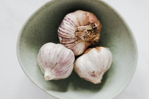 From above closeup of light gray ceramic bowl with whole garlic bulbs placed on marble table