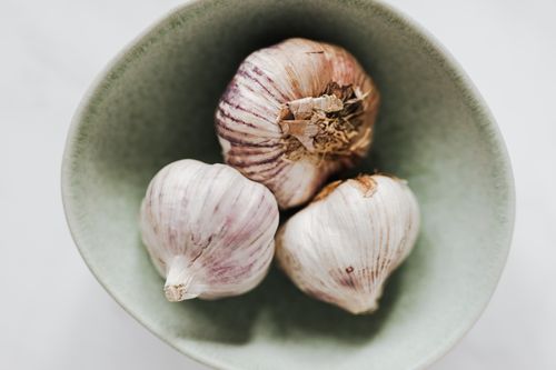 Free From above closeup of light gray ceramic bowl with whole garlic bulbs placed on marble table Stock Photo