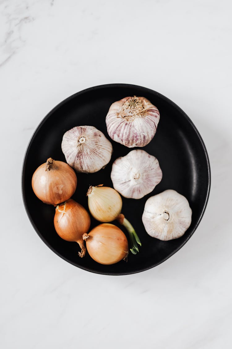 Raw Yellow Onions And Garlic Bulbs On Black Plate