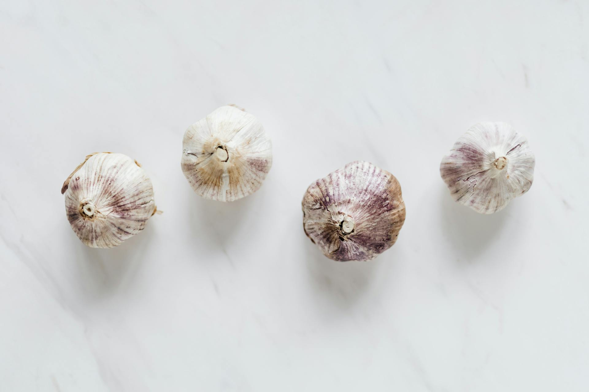 Top view of raw whole unpeeled aromatic garlic placed next to each other on white marble surface before cooking process