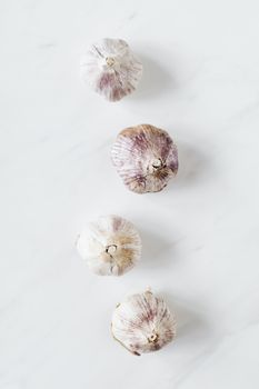 白色大理石背景上，未剥皮的新鲜大蒜鳞茎排列成锯齿形线，呈现其顶视图