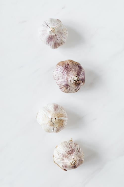 Free Top view of fresh raw aromatic unpeeled whole garlic bulbs arranged in zigzag line while placed on white marble background Stock Photo