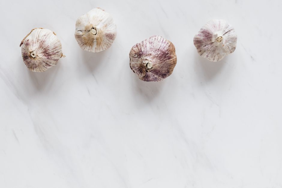 Top view of whole raw unpeeled ripe flavorful garlic bulbs composed in zigzag line and placed on white marble tabletop