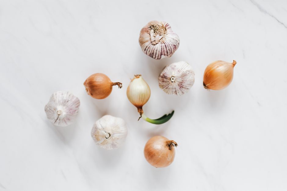 Top view composition of raw unpeeled ripe yellow onions and fresh whole aromatic garlic bulbs placed on white marble background