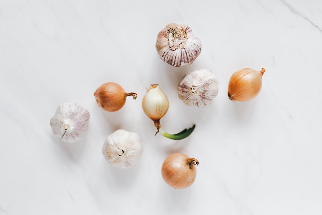 Free Top view composition of raw unpeeled ripe yellow onions and fresh whole aromatic garlic bulbs placed on white marble background Stock Photo