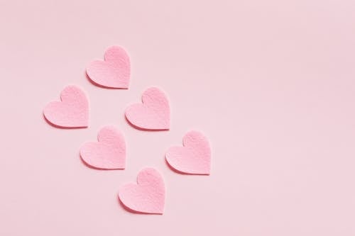 From above of composition made with heart shaped papers cutout of rough uneven pink cardboard placed diagonally on light pink background