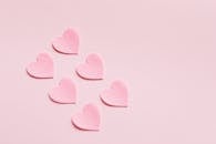 浅粉色背景上，对角放置着一个用心形纸制成的构图，由粗糙不均匀的粉红色纸板切割而成