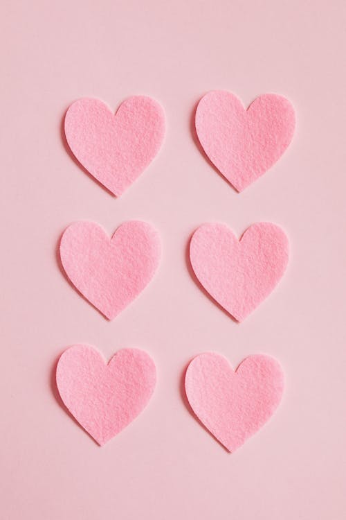 Free Top view close up composition made with bright pink hearts cut out of pink rough paper and arranged in lines on light pink background Stock Photo