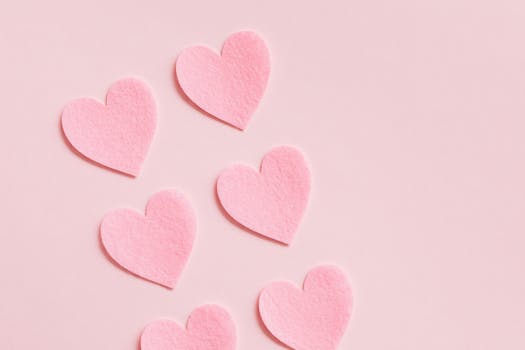 Six pink felt heart decorations arranged on a pastel pink background, perfect for romantic themes.