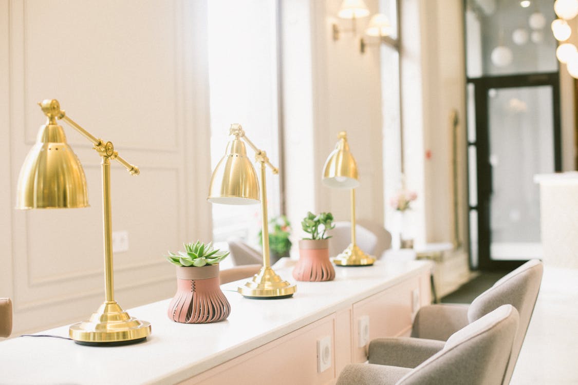 Classic interior design of stylish beauty salon with light pink desk with white desktop golden lamps and stylish plants near cozy comfortable chairs in beauty salon on sunny day