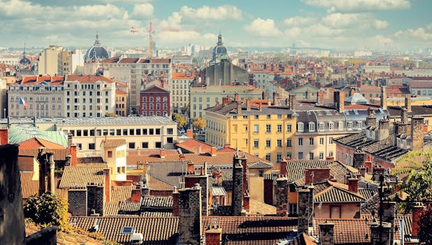 Aerial view of Lyon's historic rooftops and skyline under a bright blue sky.