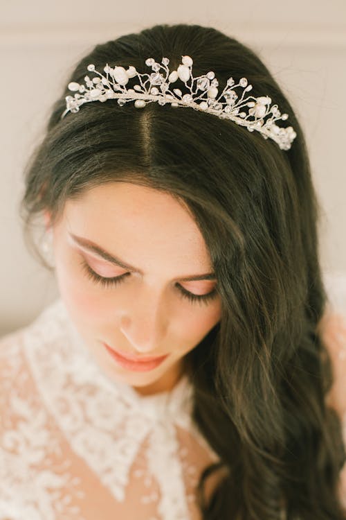Free Calm young bride wearing beautiful delicate hair accessory and white lace wedding dress and looking down Stock Photo