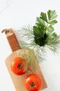 Top view of fresh ripe tomatoes placed on wooden cutting board near bunch of parsley and dill on marble surface