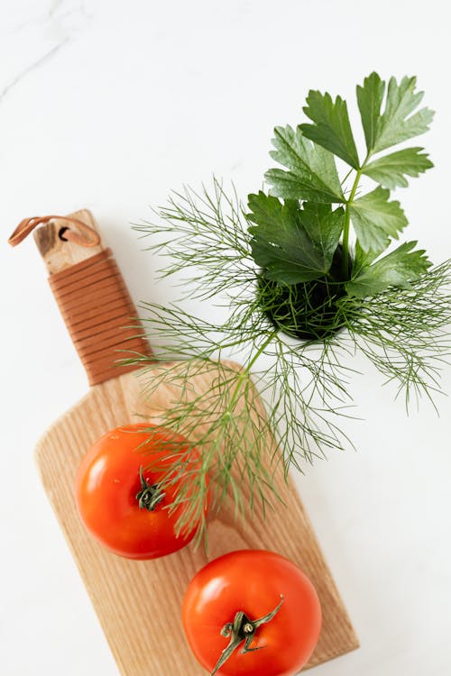 Free Top view of fresh ripe tomatoes placed on wooden cutting board near bunch of parsley and dill on marble surface Stock Photo