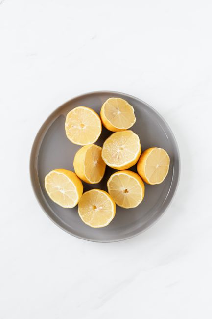 Top view of grey ceramic plate with halves of fresh ripe lemons isolated on white background