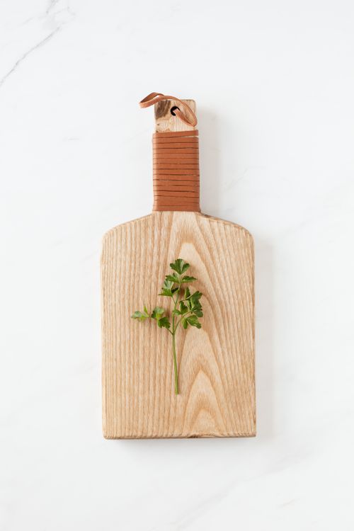 Free Overhead view of green parsley sprig lying on wooden cutting board on white marble surface Stock Photo