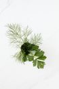 Dill and parsley sprigs in cup on marble surface