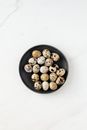 Top view of quail eggs placed in black round bowl standing on white clean marble surface
