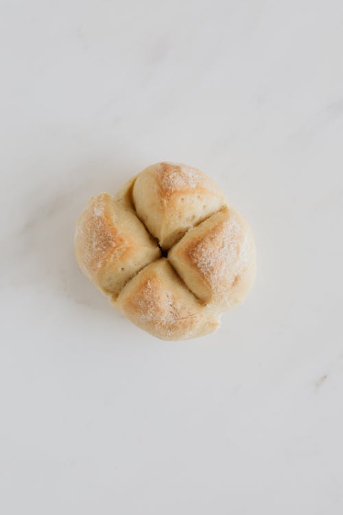 Free From above of fresh white bread bun with cross shaped cut on top lying on white marble table in soft daylight Stock Photo