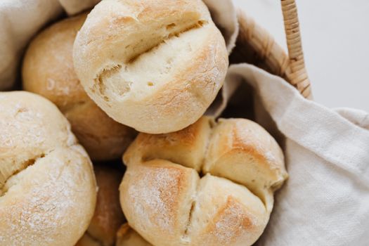 From above closeup of freshly baked delicious buns with cross cuts on top lying on linen towel in wicker bowl